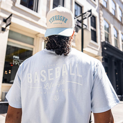 Person wearing a light blue t-shirt with 'BASEBALL Lifestyle' text and a cap in an urban setting.