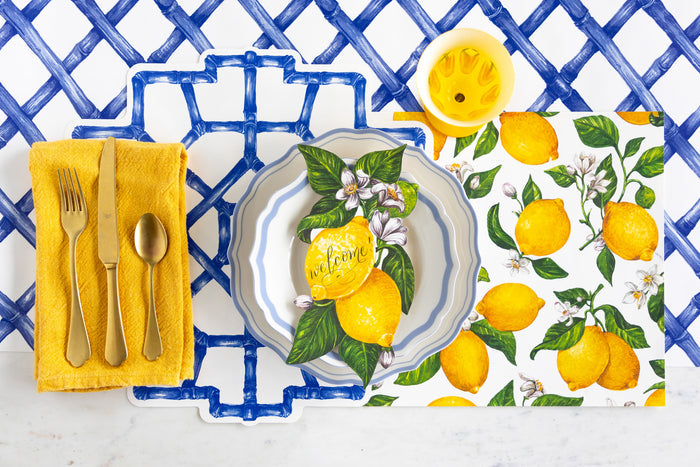 Table setting with the Die-cut Blue Bamboo and Lemons Placemats, Lemons Table Accent, Cornflower Blue Icing on the Cake plates, gold flatware and yellow napkin on the Blue Lattice Runner.