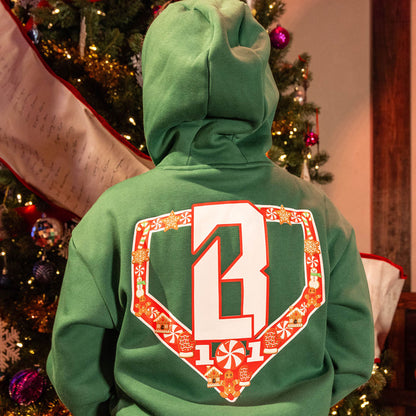 Person wearingGreen hoodie with a festive red and white BL101 logo on back in front of a decorated Christmas tree.