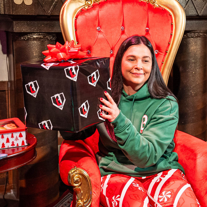 Person holding a large gift box with a red bow on a red throne-like chair.