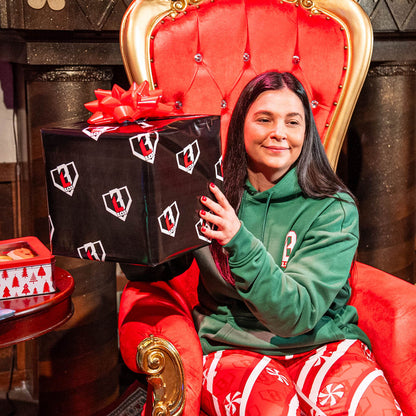 Person holding a large gift box with a red bow on a red throne-like chair.